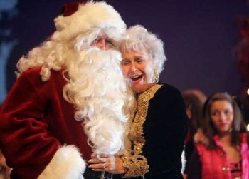 A woman smiles as she hugs Santa. Audience members look on.