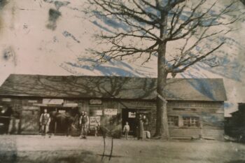 Photo of men and boys standing in front of a blacksmith shop.