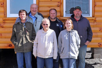 A group of men and women smile in front of a cabin after the tour.