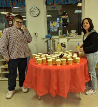 Two teenaged volunteers serve cocoa and cookies. 