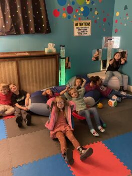 Children relax in the senory room, with calm blue walls, soft lighting, beanbag chairs and a lava lamp.