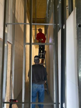 A volunteer on a ladder and a volunteer standing on the ground work to frame walls. 