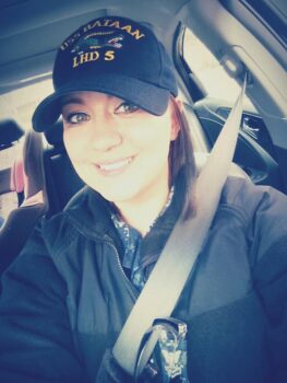 Selfie of Brooke wearing a USS Bataan LHD 5 hat and camos under a dark jacket. She is a white woman with brown hair, green eyes and a smile.