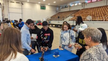 A student tries out a robot while Dr. Elizabeth Azhikannickal, director of engineering technologies at Marion Tech, and other students and educators look on.