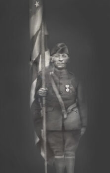 James Kasotis stands in his WWI uniform while holding a flag with his purple heart pinned to his chest. 