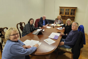 The board members smile while looking around a conference table.