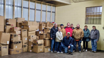A group of volunteers stands and smiles in front of a wall of boxes taller than they are in a warehouse.