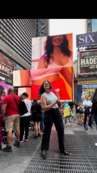 Kara smiles in front of her giant electronic billboard in Times Square. 
