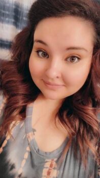 Kimberly is a fair-skinned woman with long, auburn, wavy hair, brown eyes and a slight smile. She owns Luminous Occasions event planning and Kitty Kat Candles.