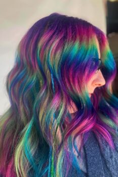 After the appointment, the client shows long, wavy hair with a mix of purple, hot pink, blue, and green blended across her hair.