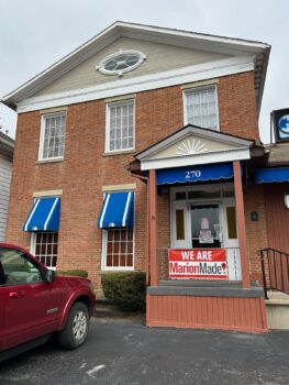 The brick two-story home with white trim is now used by Laipply's Printing & Marketing. It has a blue awning and a large "We are MarionMade!" banner on its porch. 