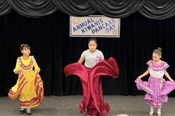 Three girls in colorful traditional clothes do a traditional Hispanic dance.