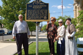 Four People stand next to the historical marker on a sunny day. 