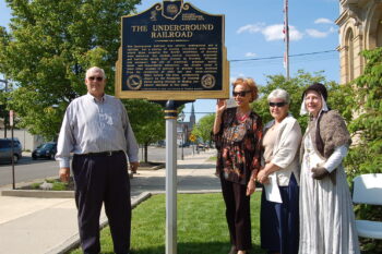 Four People stand next to the historical marker on a sunny day.
