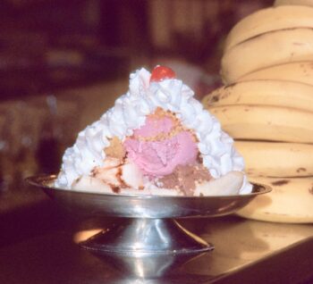 A metal dish holds bananas, eight scoops of ice cream, four types of syrup, whipped cream and a cherry. 