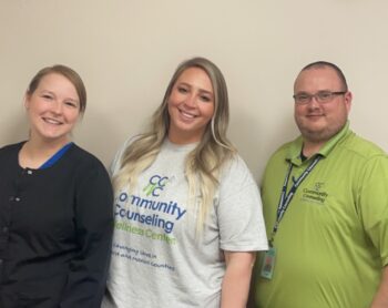 The Crawford team members smile. Amanda is a white woman with dark blonde hair in a pony tail and navy scrubs covered by a black jacket. Lexi is a white woman long wavy blonde hair and a gray CCWC T-shirt. Dustin is a white man with buzzed, dark hair, facial hair and glasses. He is wearing a green CCWC polo and has  a lanyard with his employee badge. 