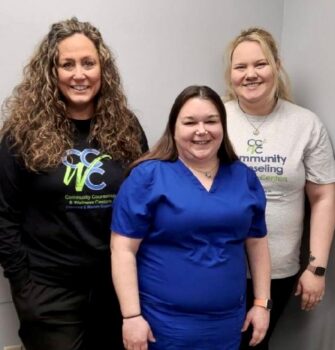 Photo of the three staff members smiling. Any is a tall white woman with long, brown, curly hair and a black CCWC sweatshirt. Anni is a short woman with long, straight brown hair and navy blue scrubs. Ashley is a tall white woman with blonde hair in a pomy tail and a gray CCWC T-shirt.