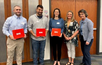 The new members smile next to the leadership team. The new members have BNI welcome kits.