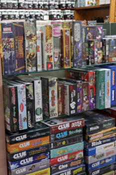 A shelf full of board gmaes including Operation, Clue, and Monopoly. Miniatures are visible in the background
