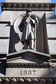 A gray statue on the front of the Soldiers' and Sailors' Chapel shows a Union Solder with a uniform including a belt stating U.S. and holds a musket while leaning forward. Below the figure, 1887 is carved into the stone.