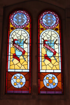 Stained glass windows have the letters US entwined at the top, surrounded by stars. Below is a shieled with a ribbon stating "Union". 