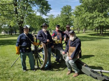 Five men in navy blue historical garb pose next to a large canon at Veterans Park in Marion, Ohio. 
