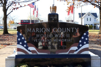 A black stone memorial is enscribed: Marion County World War II Veterans Memorial. Dec. 7, 1941 to Dec. 31, 1946. It has a red white and blue flag carved into the stone. On top there is a gilded eagle on top of a smaller black stone with the word "Honor" and a single star.