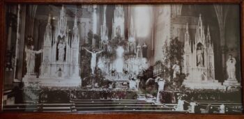 A black and white photo of a church with large white statues, a crucifix and wooden pewes.