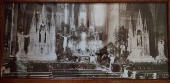 A black and white photo of a church with large white statues, a crucifix and wooden pewes. 