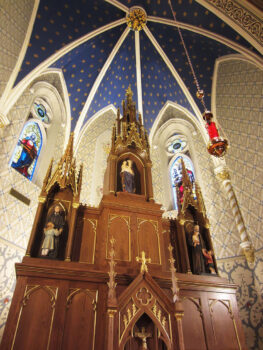 A close-up look at the church's statuses, wooden altera with a crucifix and gold details, stained glass windows, and high ceilings.