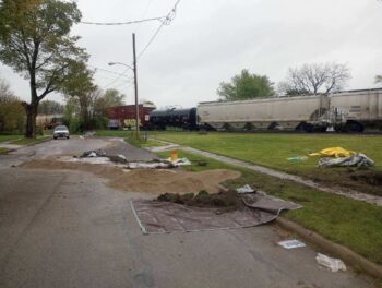 STopped Train cars in the background. Sand and tarps are piled in teh street on the neighboring road.