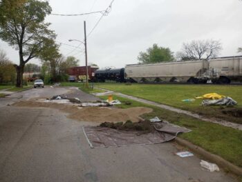 STopped Train cars in the background. Sand and tarps are piled in teh street on the neighboring road. 