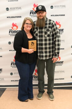 A winner of the Alluvial Private Wealth Forge Competition smiles and holds a wooden plaque next to a supporter.