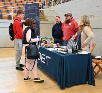 Three adults at a booth talk to students.