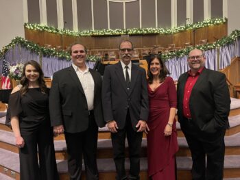 Four soloists and the director in suits or formal long dresses smile at the front of the church after the 2022 performance.