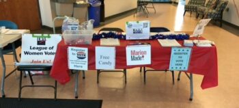 A table with MarionMade! and League of Women Voters signs and information. in the lobby of a local community college. 