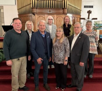 The board stands in front of a church organ and smiles.