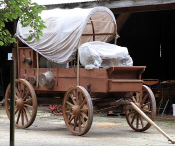 A wooden covered wagon with wooden wheels and a white cloth covering.