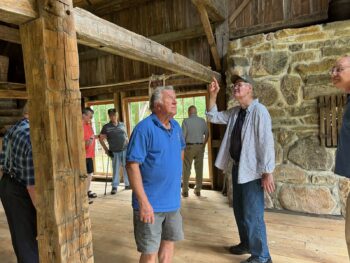 Dennis points to a beam inside the Grist Mill. wooden mbeams are around light streams in from large glass doors.