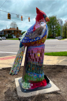 A cardinal with deisgns of stars, owls, flowers, and feathers stands.