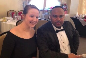 A white woman and a black man in formal dress smile at a banquet.