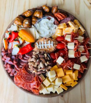 A tray for a super bowl party includes nuts, a cheese ball in the shape of a football, stuffed peppers, pretzel bites and more. 