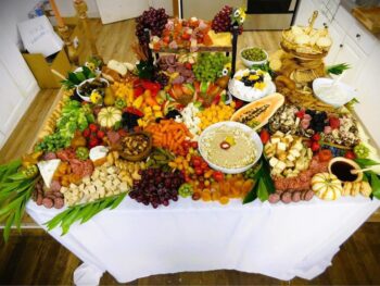 A table is filled with layers of food including fruits, meats, cheeses, dips, bread, crackers, olives, and fresh fruit. 