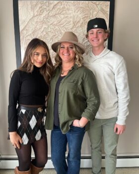 Leiha stands in the center next to her children, a young woman with long brown hair and a teenage boy with a backwards hat and short, blonde hair. 