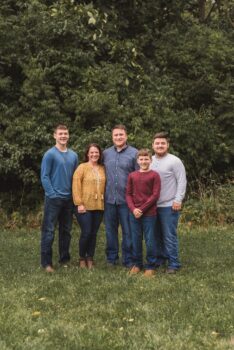 The family stands in a field and smiles. 