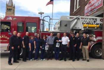 Firefighters, doctors and staff stand in front of a fire truck. 