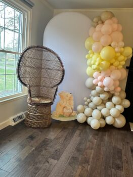 A wicker chair stands in front of a balloon sculture and a figure of Winnie the Pooh.