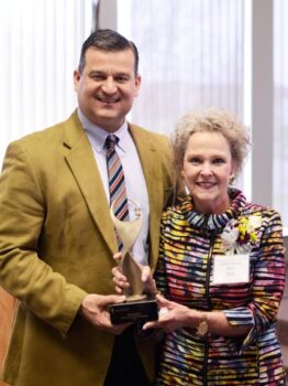 The mayor, a white man with short brown hair and a suit, hands Pam the gold award statue. 