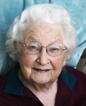 A close up of Dorothy, a white woman with short, white, wavy hair, gold-rimmed oval glasses, blue eyes, and a smile.