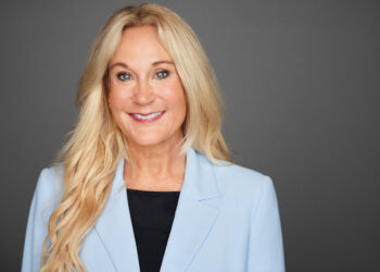 Jill Frey smiles. She is a white woman with long, blonde, wavy hair; blue eyes, a smile, a black shirt with a powder blue suit jacket and delicate gold earings.